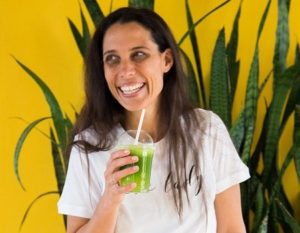 Catherine Morris smiling and holding a smoothie cup with paper straw and green juice