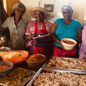 Mama Mickey and some of her volunteers with big trays of cooked food