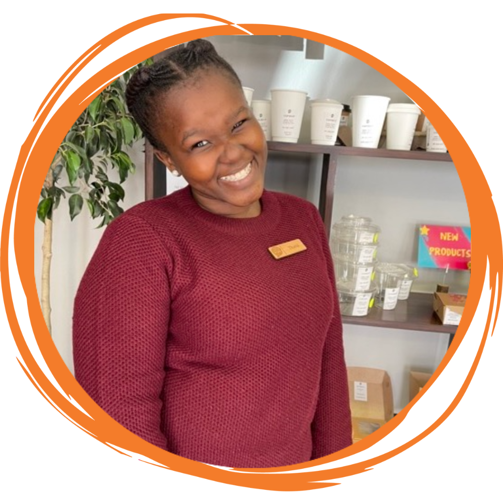 Thato smiling in front of compostable packaging samples in the showroom