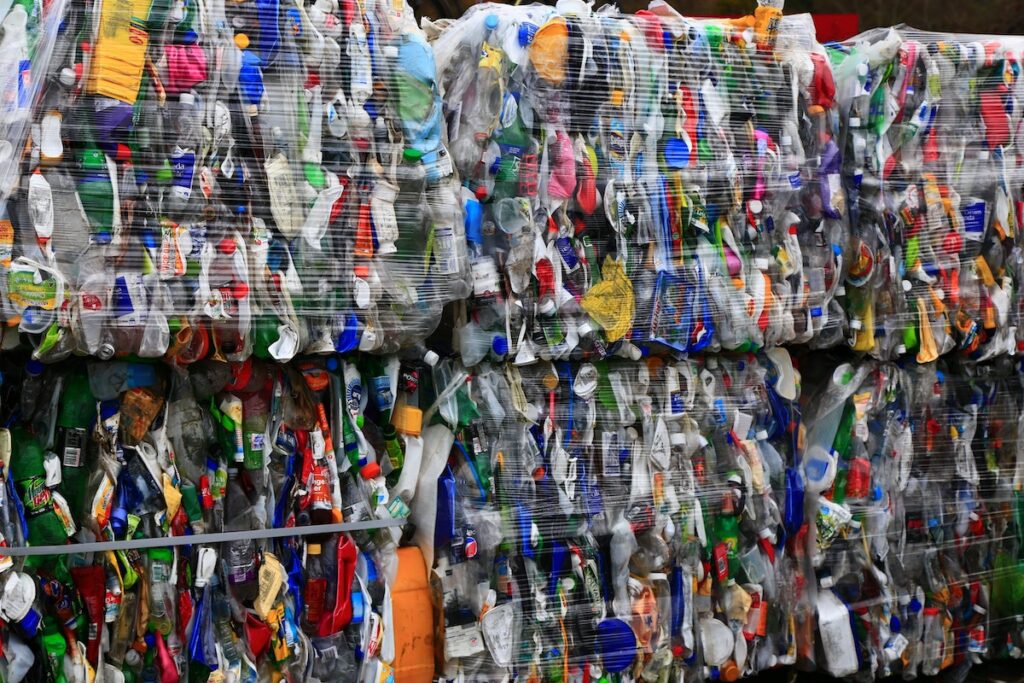Bales of collected and crushed plastic waste in many colours for recycling, wrapped in clear plastic wrap