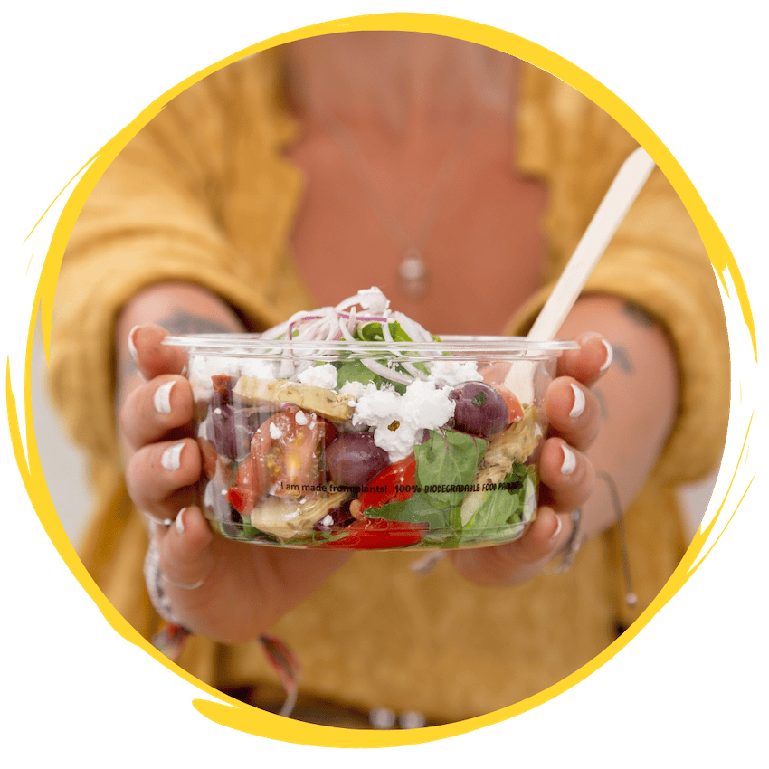 hands holding a clear bioplastic bowl full of salad